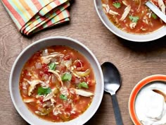 a bowl of soup on a table with two spoons next to it and another bowl of sour cream