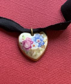 Gorgeous antique choker in good condition! This beautiful piece is believed to from the early 1900's. It features a ceramic heart with hand painted pink, white and blue flowers. It has a golden painted outline and measures 7/8 of an inch high. The back of the pendant does show a bit of wear on the plaster. The black ribbon measures 22 inches long and is 3/8 of an inch wide. Please note that is does not lay entirely flat. What a unique and wonderful find! FREE SHIPPING ON ALL OUR ITEMS!! Orders are shipped out within 24 hours of payment Monday- Saturday (excluding Holidays) For my international buyers: Yes, I do combine shipping :) THANK YOU FOR STOPPING IN AT CAMI JUNE'S VINTAGE! Fabric Choker Necklace, Blue Flower Fabric, Fabric Choker, Antique Choker, White And Blue Flowers, Ceramic Heart, Flower Fabric, Ribbon Necklace, Rose Blue