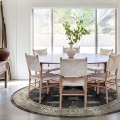 a dining room table with chairs and a potted plant in the center on a rug