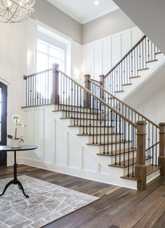 a room with a table, rug and stairs in the middle of it on top of a hard wood floor