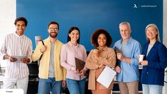 a group of people standing next to each other in front of a blue wall holding papers