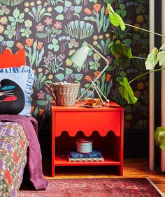 a bedroom with colorful wallpaper and a red nightstand next to a green potted plant