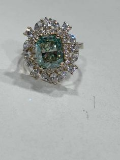 a fancy ring with an aqua blue diamond surrounded by white and clear stones on a plain surface