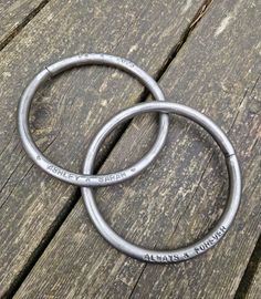 two metal rings sitting on top of a wooden table next to each other with the words always a nice day written on them