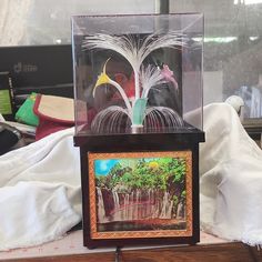 a wooden table topped with a glass case filled with pictures and artwork next to a window