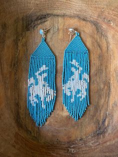 two blue and white beaded earrings sitting on top of a wooden table