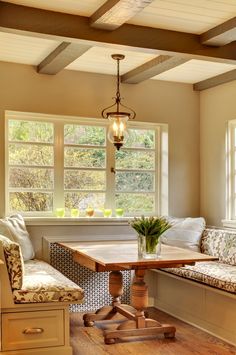 a table with two chairs and a bench in front of a window that has flowers on it