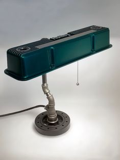 a green table lamp sitting on top of a metal base with a cord attached to it