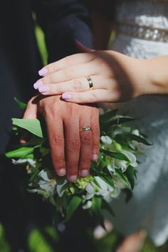 two people holding each other's hands with wedding rings on their fingers in front of flowers