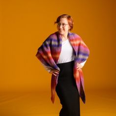 a woman is standing in front of an orange background wearing a multicolored shawl