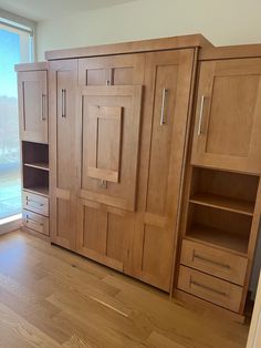 an empty room with wooden cabinets and hard wood flooring, large window in the background