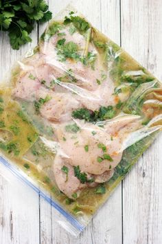 chicken breast wrapped in plastic sitting on top of a wooden table next to parsley