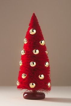 a red christmas tree with gold balls on it's top and bottom, in front of a gray background