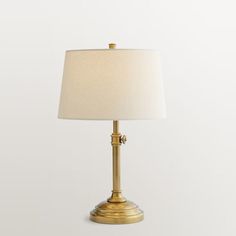 a gold lamp with a white shade on it's base and an off - white background