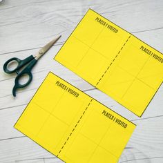 two pieces of yellow paper with scissors next to them on a white wooden table,