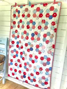 a red, white and blue quilt hanging on the side of a wall next to a chair