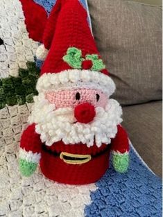 a crocheted santa clause sitting on top of a couch next to a pillow