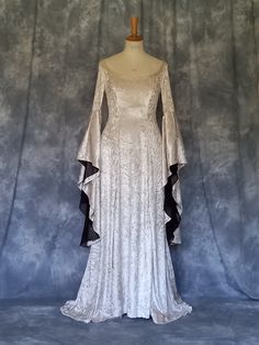 Medieval Gown,Elvish Dress,Celtic Gown,Custom Made,Hand Fasting Dress,Robe Medievale,Robe Elfique,Renaissance Dress,Elvira. Elvira, a medieval wedding dress, elegant styled in silver crushed velvet. Back corset style lacing allows for a little adjustment. The inner sleeves are in a soft organza. Elvira is also pictured with a cloak, made for a client for a Halloween wedding. It is designed and custom made by Gill Linley of frockfollies. Perfect as a Hand Fasting Dress or an Elvish Wedding Dress. CHECK OUT http://www.frockfollies.com for other designs and colour choices. FREE INSURED AND TRACKABLE SHIPPING Hand made in England by an experienced theatrical costumier, this medieval gown Elvira is available to order in a wide choice of colors and will be custom made to your measurements.  froc Elven Style Wedding Dress With Historical Design, Elven Wedding Dress With Historical Design, Medieval Wedding Dress With Historical Design, Elegant Floor-length Medieval Dress For Festivals, Gothic Historical Wedding Dress, Fitted Medieval Floor-length Gown, Medieval Style Fitted Floor-length Gown, Elegant Floor-length Medieval Dress, Fitted Elven Medieval Dress Floor-length