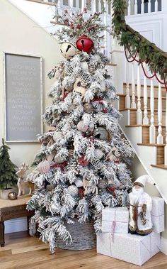 a white christmas tree with red and silver ornaments in a basket on the floor next to stairs