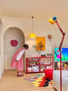 a woman in a pink dress is looking at a television screen with a lamp on it