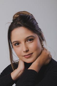 a woman with her hand on her chin and looking at the camera while wearing a black sweater