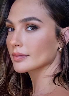 a close up of a woman with long hair and blue eyes wearing gold hoop earrings