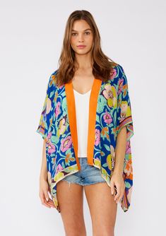 [Color: Blue/Coral] A front facing image of a brunette model wearing a bohemian style kimono top in a bright blue and coral floral print with a contrast orange border. A lightweight beach cover up with half length kimono sleeves Blue Floral Print Cover-up For Spring, Blue Floral Print Spring Cover-up, Spring Blue Floral Print Cover-up, Blue Wrap Kimono For Beachwear, Vibrant Spring Kimono With Vibrant Print, Blue Floral Print V-neck Cover-up, Blue V-neck Cover-up With Floral Print, Blue V-neck Floral Print Cover-up, Blue Boho Print Kimono For Spring