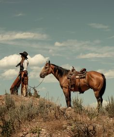 two men in cowboy hats standing on top of a hill next to their brown horses