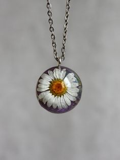 a white and yellow flower is in a glass ball on a silver chain that hangs from a necklace