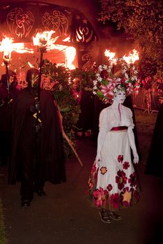 two people dressed up in costumes with fire coming from behind them at an outdoor event