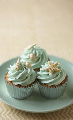 three cupcakes with green frosting and starfish decorations on a blue plate