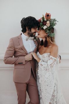 two people standing next to each other in front of a white wall with flowers on their head