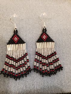 a pair of black and red beaded earrings sitting on top of a gray surface