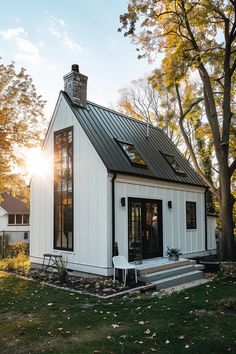 a small white house with a black metal roof and windows on the front porch, surrounded by trees