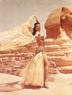 a woman in a long dress standing next to an egyptian pyramid