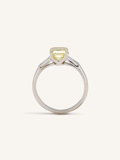 Vintage Art Deco engagement ring centered with a 1.86 carat Fancy Intense Yellow diamond elegantly accented by pair of slender baguette diamonds and a platinum band with sleek lines and a beautifully fine low profile. Fancy Intense Yellow diamonds, also known as "Canary diamonds", are prized for their vibrant, sun-drenched hue. These diamonds are unique due to their intense color saturation, which is a result of the presence of nitrogen molecules that absorb blue light, thus giving the diamond its yellow color. Unlike other diamonds, the value of Fancy Intense Yellow diamonds increases with the richness and purity of their color, rather than their lack of color. Their dazzling yellow hue, combined with the natural brilliance of a diamond, creates a stunning visual impact that is both disti Timeless Gia Certified Baguette Cut Diamond Ring, Timeless Baguette Cut Gia Certified Diamond Ring, Timeless Asscher Cut Baguette Diamond Rings, Timeless Platinum Baguette Cut Diamond Ring, Timeless Asscher Cut Ring With Baguette Diamonds, Timeless Asscher Cut Rings With Baguette Diamonds, Classic White Gold Baguette Cut Diamond Ring, Classic Emerald Cut Baguette Diamond Wedding Ring, Gia Certified Classic Baguette Cut Diamond Ring