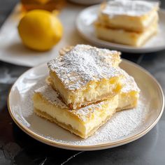 three pieces of cake on a plate with powdered sugar and lemons in the background