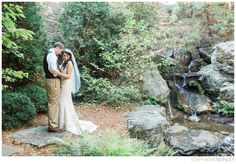 a bride and groom standing in front of a waterfall