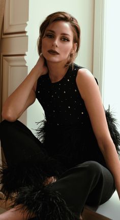 a woman is sitting on the floor with her legs crossed, wearing black feathers and heels