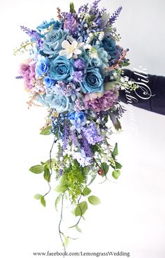 a bridal bouquet with blue flowers and greenery on the bottom is being held by someone's hand