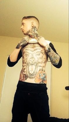 a man with tattoos on his chest is standing in front of a mirror and looking at himself