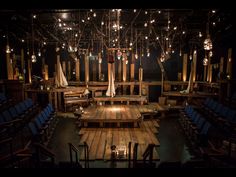 an empty stage with blue chairs and lights hanging from the ceiling, surrounded by wooden planks