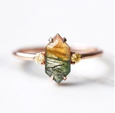 a gold ring with a green and yellow stone on it's side, sitting on top of a white surface