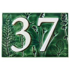 a green ceramic house number sign with white numbers and plants on it's side