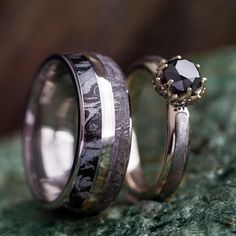 two wedding rings with black and white diamonds on them sitting on green mossy ground