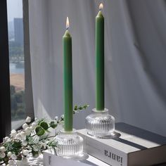 two green candles sitting on top of a table next to a box with flowers in it