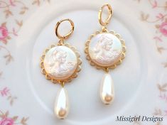 These beautiful cameo earrings were created with ornate brass settings adorned with white pearlescent Cameo cabochons and vintage teardrop pearls. These earrings hang beautifully from gold plated lever back ear wires and measure 2 1/4 inches in length and 7/8 inches in width. ~All of my listings are handmade with love and ready to ship and will arrive to you in a gift box with bow for easy gift giving~ Elegant Cameo Clip-on Earrings Gift, Cameo Drop Earrings For Wedding, Gold Cameo Earrings For Wedding, Elegant Cameo Earrings For Wedding, Elegant Round Cameo Earrings, Victorian Dangle Pearl Earrings, Victorian Pearl Earrings For Pierced Ears, Elegant Cameo Dangle Earrings, Antique Pearl Drop Earrings As Gift