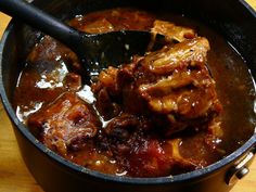 a pot filled with meat and sauce on top of a wooden table