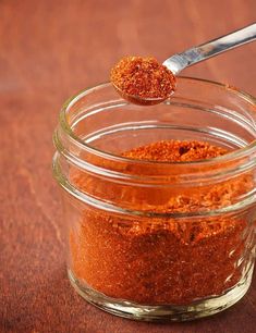 a jar filled with red chili powder and a spoon full of seasoning next to it