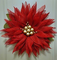 a red and gold poinsettia hanging on a door with two balls in the center